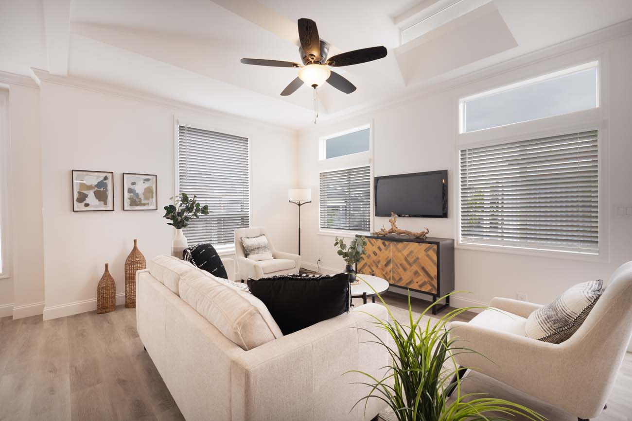 Living room with large windows, white seating, and wall-mounted television