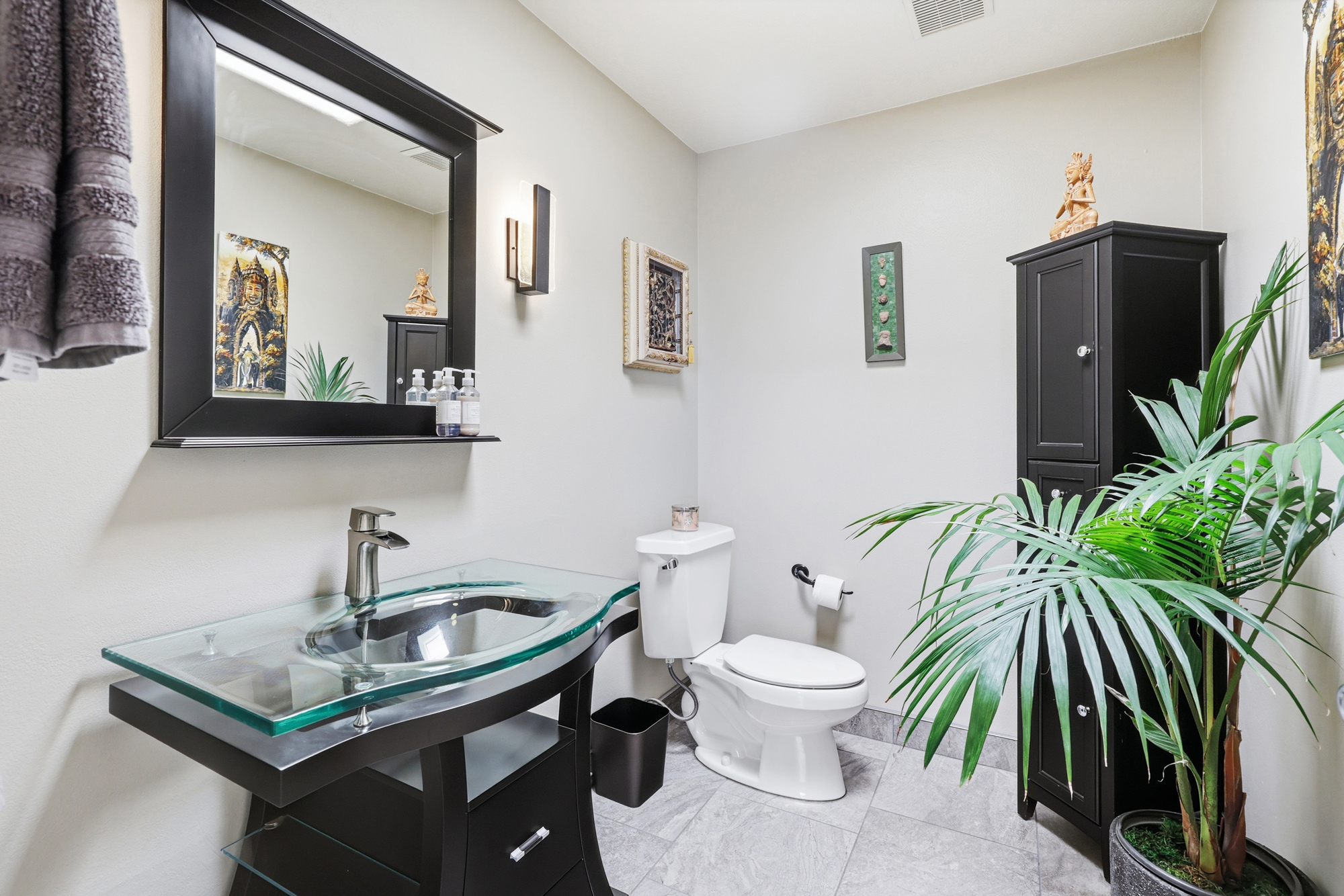 Commercial restroom with glass vessel sink, black vanity, toilet, and indoor plants