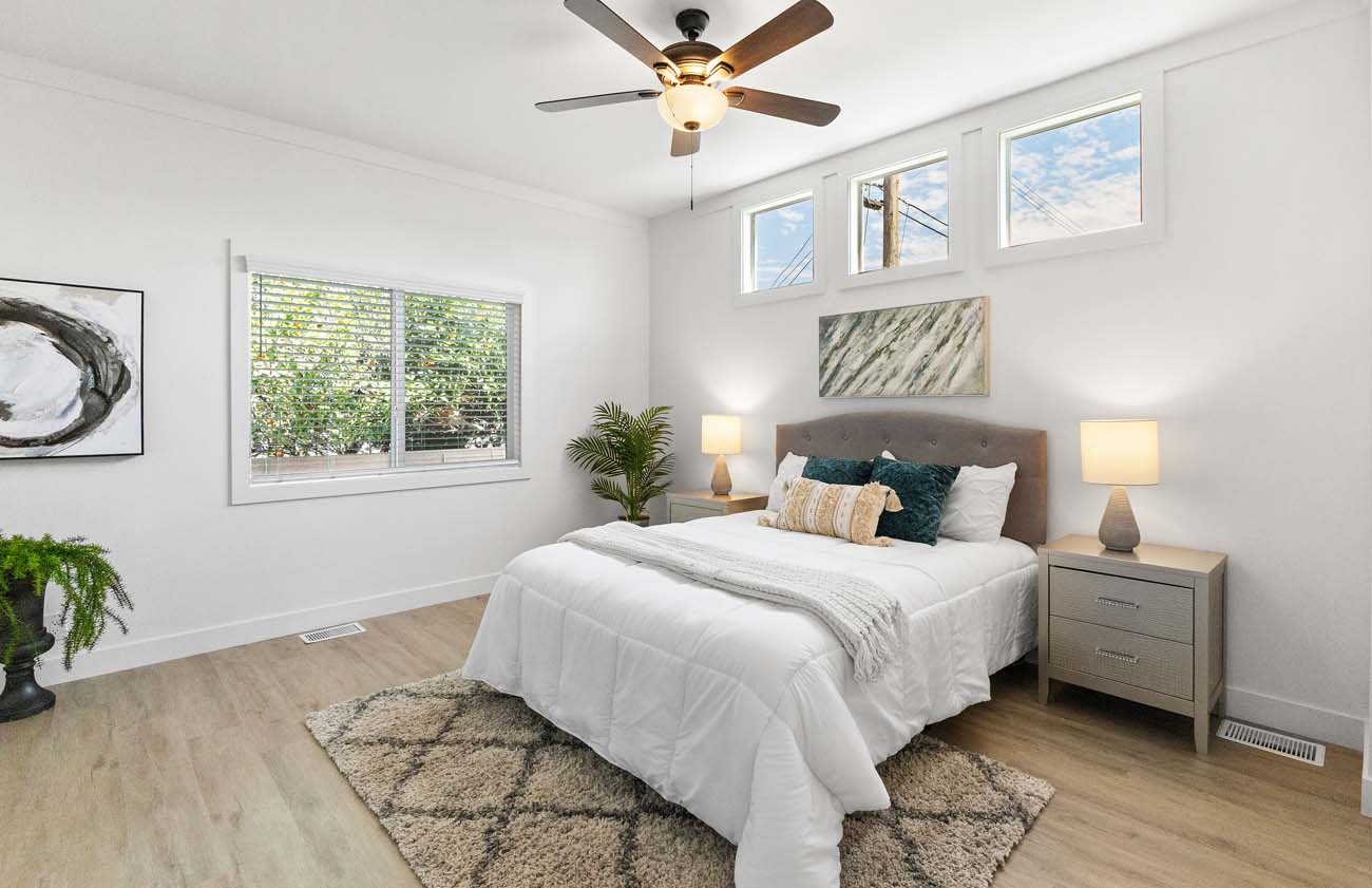 Bright primary bedroom with white furnishings, ceiling fan, and clerestory windows
